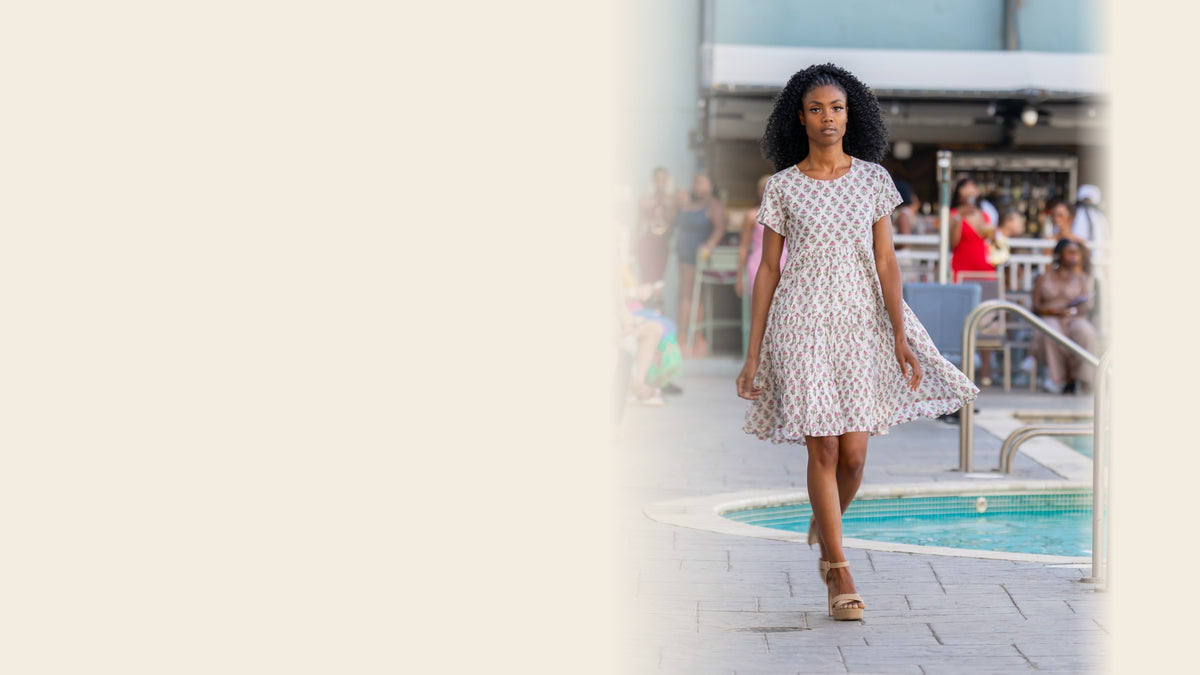 Model walking a poolside runway in the Mapulder Anna Dress, a hand block-printed cotton dress with a small pink floral print